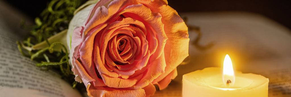 Eine Rose und eine Kerze liegen auf einem geöffneten Buch Eine Rose und eine Kerze liegen auf einem geöffneten Buch